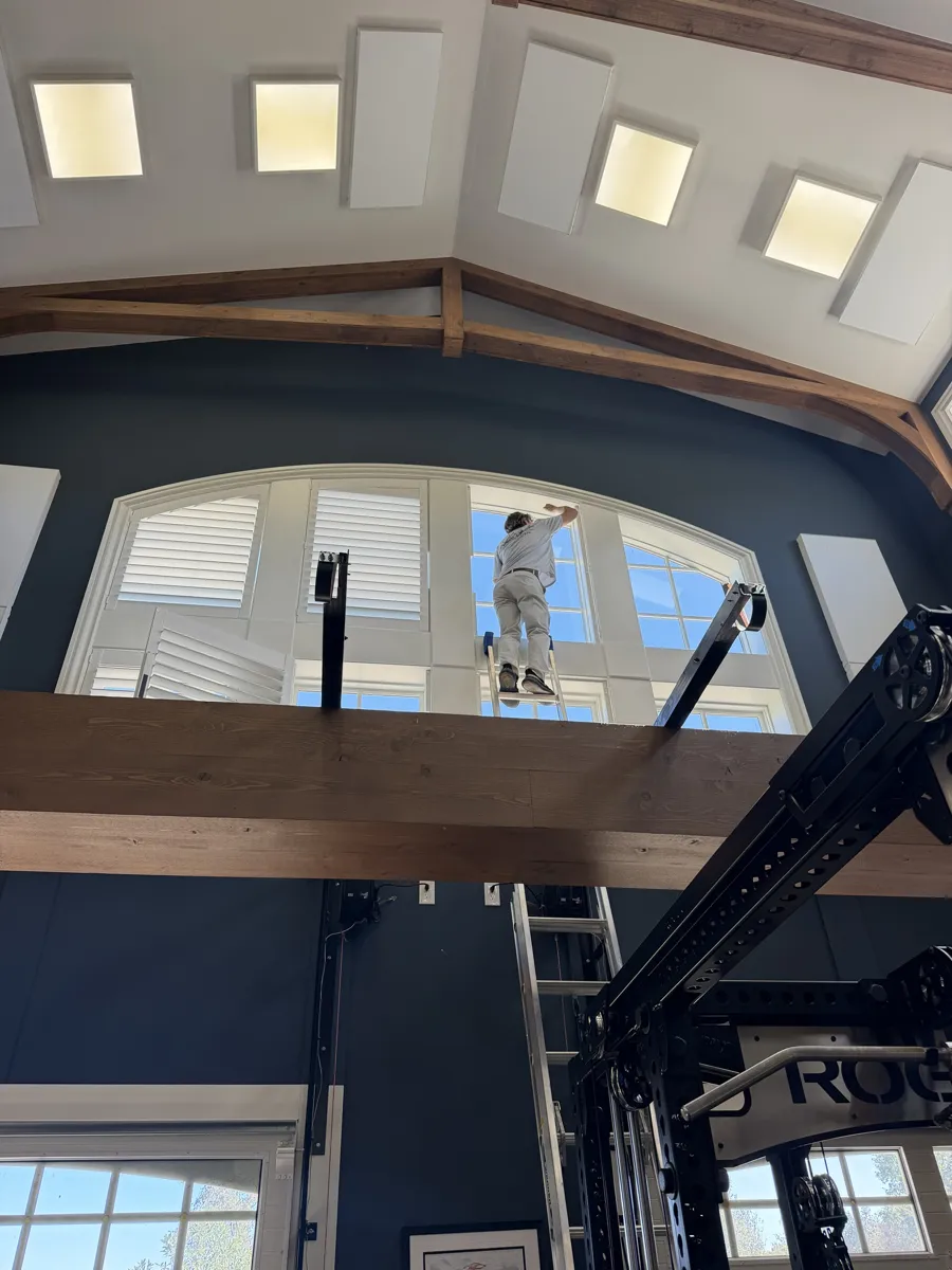 Installer on a ladder fitting custom plantation shutters on a two-story arched window wall in a Delaware, Ohio home