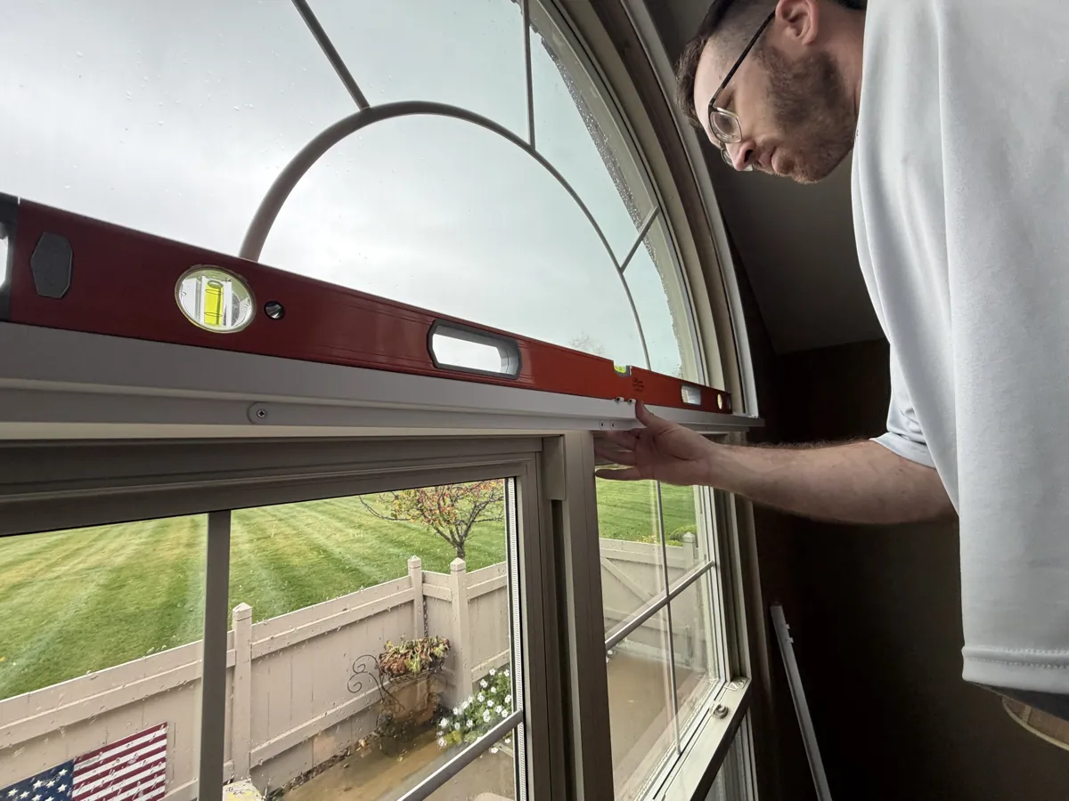 Installer leveling a shade headrail on a double-hung window below an arched window in a Lancaster, Ohio home